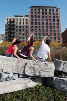 Rear view of a man with two women exercising on a rock