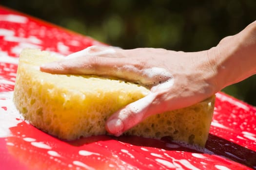 Close_up of a personŽs hand cleaning the car with a bath sponge
