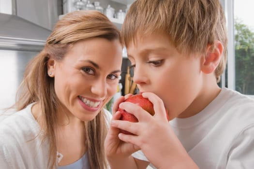 Boy eating an apple and his mother smiling