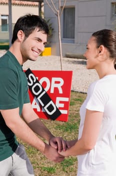 Young couple holding hands of each other in front of a sold information board
