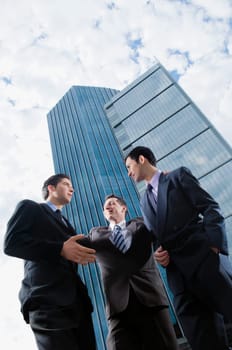 Low angle view of three businessmen discussing in front of skyscrapers