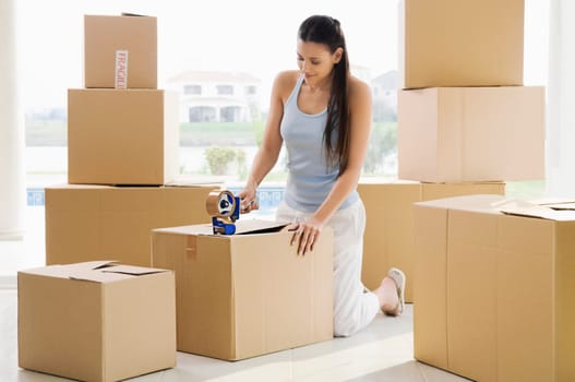 Young woman pasting adhesive tape on a cardboard box