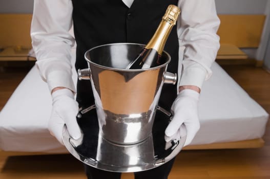 Mid section view of a waiter holding a champagne bottle in an ice bucket