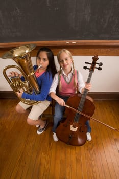Two schoolgirls playing a cello and a tuba in a classroom