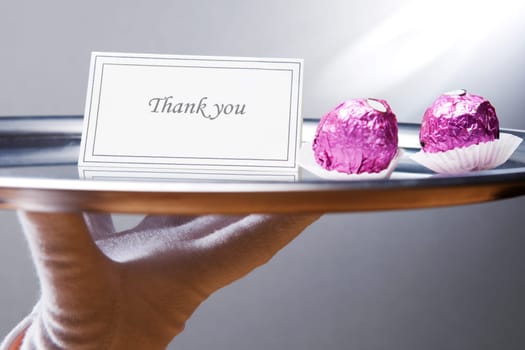 Close_up of a waiterŽs hand carrying a plate with thank you note and chocolates