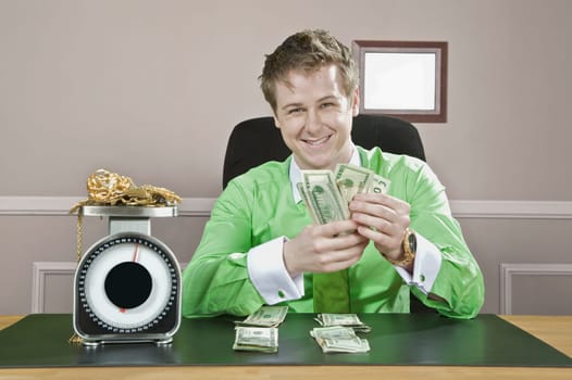 Businessman holding currency notes with gold jewelry on a weight scale in front of him