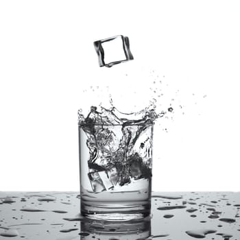 Splashing water. Glass with water or alcohol with splashes from falling ice cubes isolated on white background