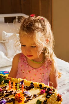 Baby girl sitting on the bed with a birthday cake
