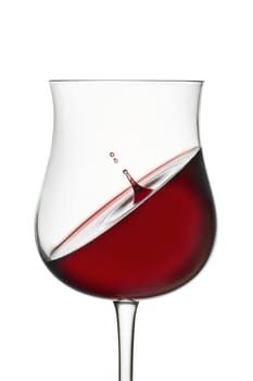 Splashing in glass. Red wine in wineglass isolated on white background. Drop falls into glass and creates splash and wave on surface of red wine