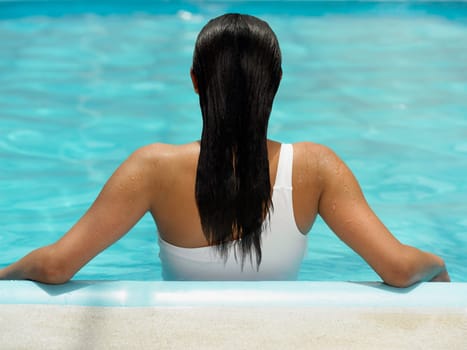 Rear view of a woman leaning against the side of a swimming pool