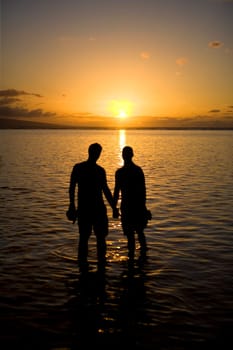 Silhouette of two gay men standing in water at sunset, Maui, Hawaii, USA