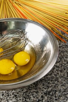 Egg yolk and an egg beater in a bowl with spaghetti