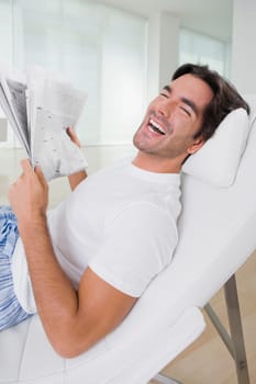 Young man holding a newspaper on a reclining chair and smiling