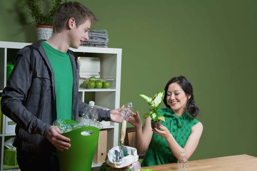 Woman showing a seedling to a man holding a recycling bin beside her