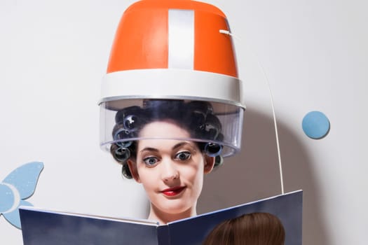Close_up of a young woman sitting under hair dryer and reading a book