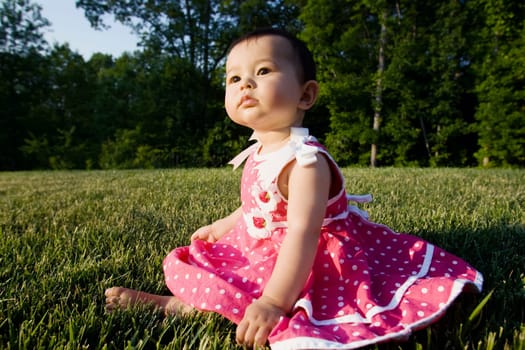 Close_up of a baby girl sitting on grass in a park