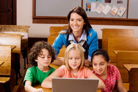 Students with their teacher using a laptop in a classroom