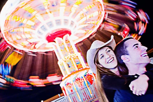 Teenage girl embracing a teenage boy in an amusement park and smiling