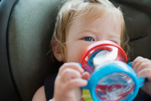 Close_up of a baby girl drinking water from a baby bottle