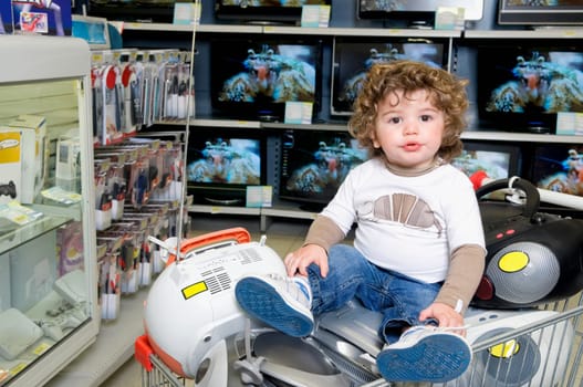 Baby boy sitting on a shopping cart in a supermarket