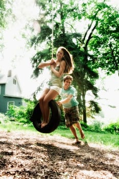 Teenage girl swinging on a tire swing with a young man pushing her
