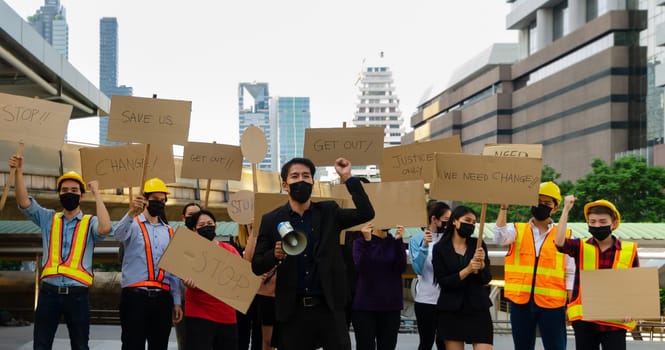 Group of people in different career wearing protective face mask protesting and raising banners in the city for justice and equal rights . A man in black suit with raising hand and holding megaphone, demonstration concept.