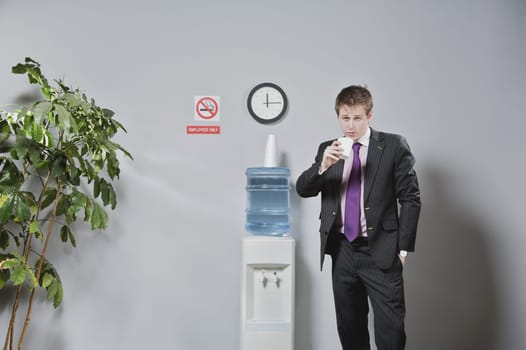 Portrait of a businessman drinking water beside a water cooler