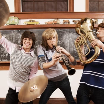 Three teenage boys playing musical instruments in a classroom