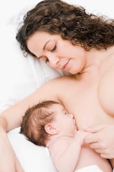 Mature woman lying on the bed and breastfeeding her newborn baby girl