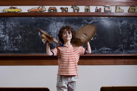 Schoolboy playing cymbals in front of a blackboard