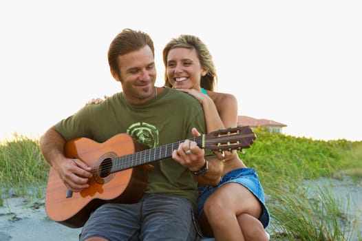 Mid adult man playing a guitar with a young woman smiling