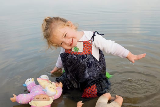 Portrait of a baby girl sitting in water with her dolls