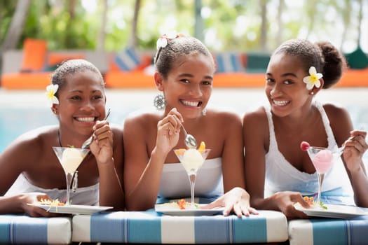 Teenage girl with her friends eating ice creams at the poolside