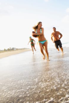 Young woman holding an American football and running on the beach