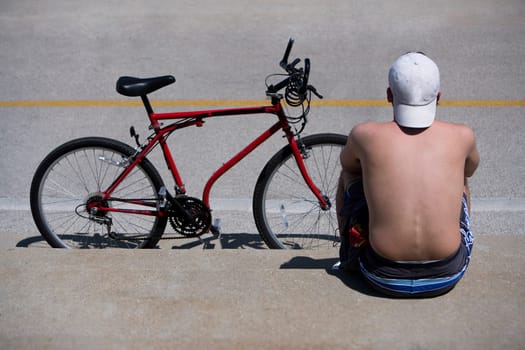Rear view of a man sitting at roadside with a bicycle, Oak Street Beach, 1000 North Lake Shore Drive, Chicago, Illinois, USA