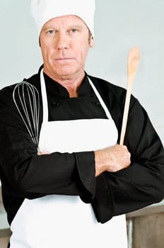 Chef holding a wooden spoon and a wire whisk