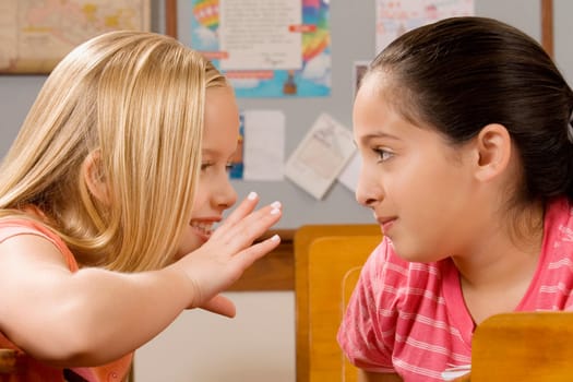 Schoolgirl whispering to her friend in a classroom