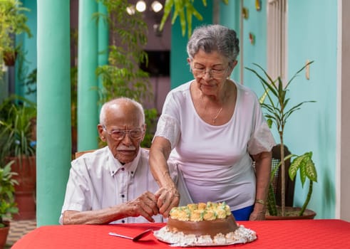 Smiling elderly couple cutting a cake helping each other