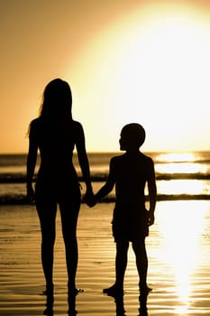 Silhouette of a woman with her son standing on the beach