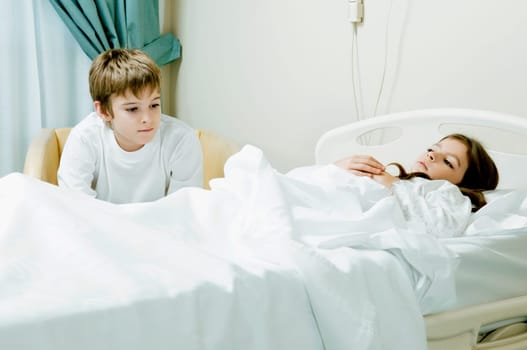 Girl on a hospital bed with her brother sitting beside her