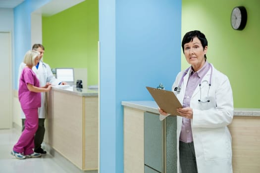 Female doctor holding a clipboard with a doctor and nurse in the background