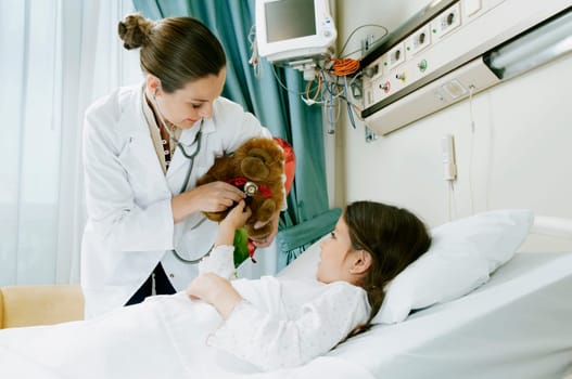 Girl on a hospital bed with a female doctor examining a stuffed toy