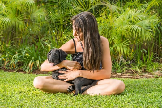 A teenage girl plays with her Labrador puppy outside on the lawn of their garden.