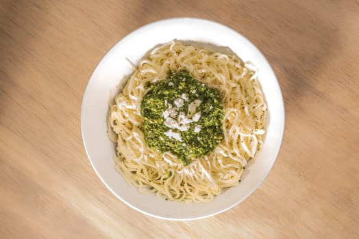Fresh Tagliatelle pasta topped with basil pesto sauce in a bowl on a wooden surface, viewed from above.