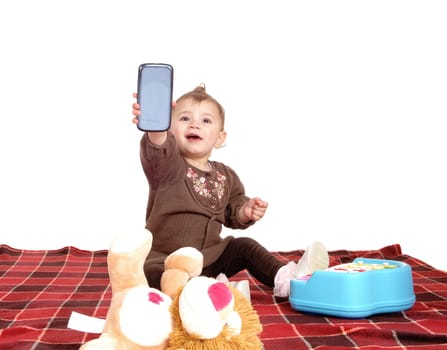 A little baby girl sitting on a blanket on the floor with her toy's and playing.with her mom's cell phone, isolated for white background..
