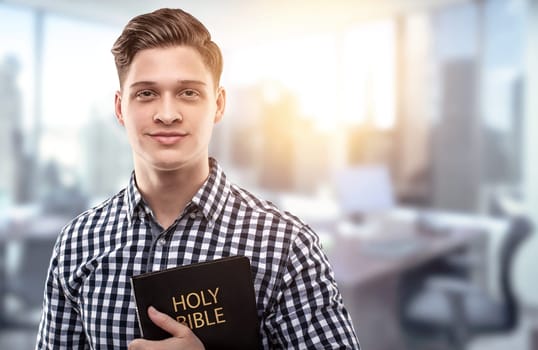 Young man holding a Bible in a modern office (concept for a successful businessman who has principles from the Holy Bible)
