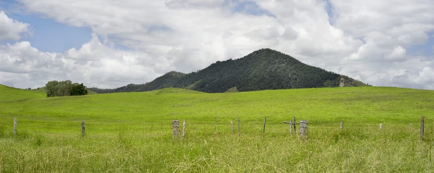 Rural Australian panorama country scene with barb wire fenceline, rolling green hills, cloudy summer sky in Queensland