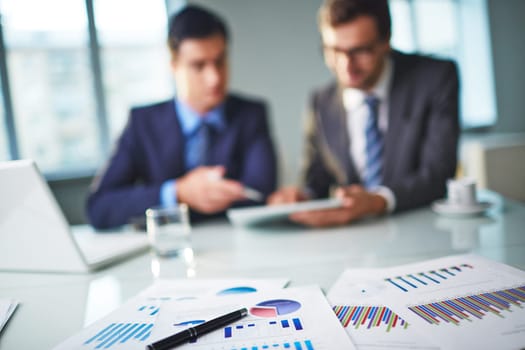 Business documents at workplace and two businessmen networking on background