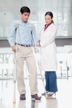Female doctor assisting a man on crutches