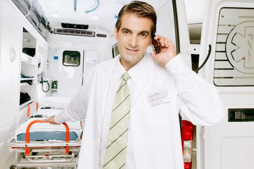 Doctor talking on a mobile phone in front of an ambulance